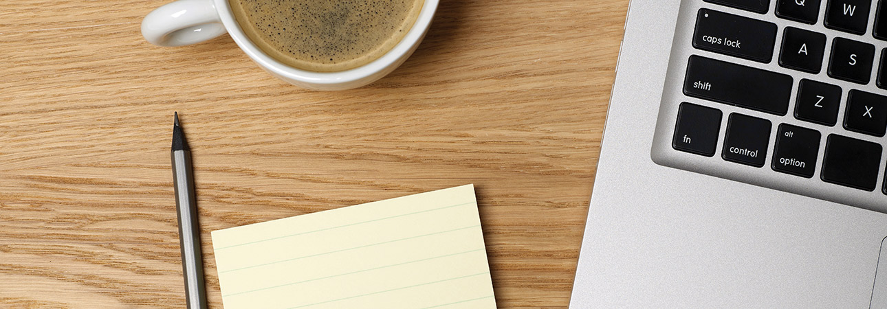 laptop on table with pen, notepad, and cup